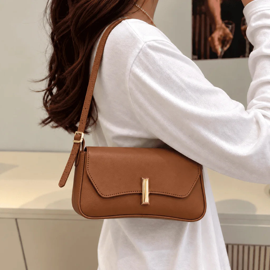 Bolsa Amélia caramelo usada no ombro, com aba curva e detalhe dourado