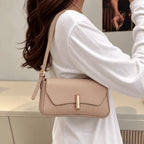 Bolsa Amélia nude usada no ombro, com aba curva e detalhe dourado