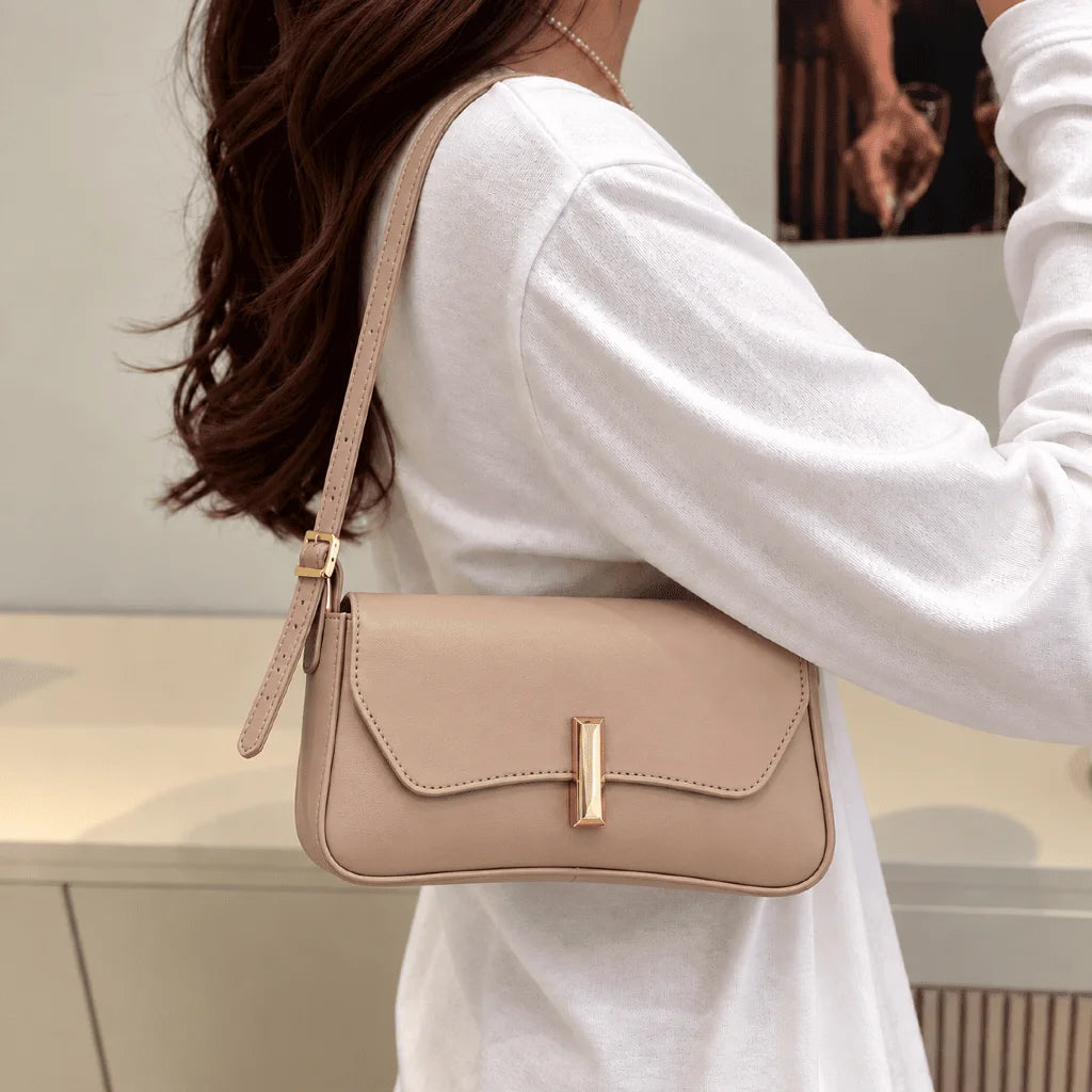 Bolsa Amélia nude usada no ombro, com aba curva e detalhe dourado