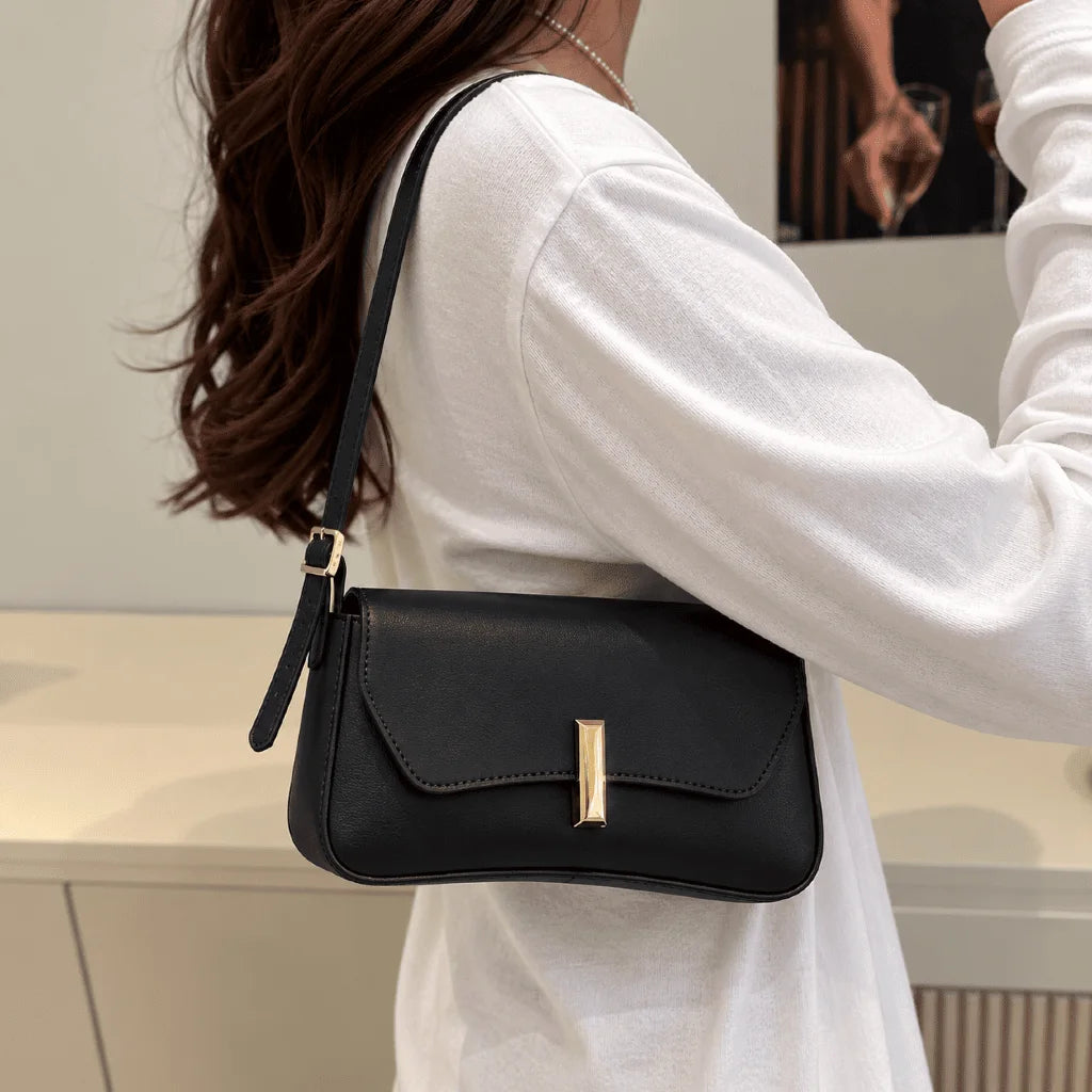 Bolsa Amélia preta usada no ombro, com aba curva e detalhe dourado